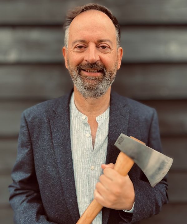 Image of Pete George holding axe in front of blurred wakk